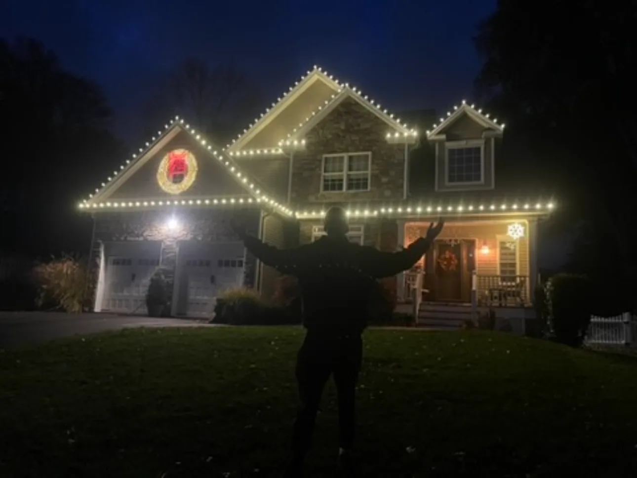 Two-story home with warm white Christmas lights along the roofline and entrance