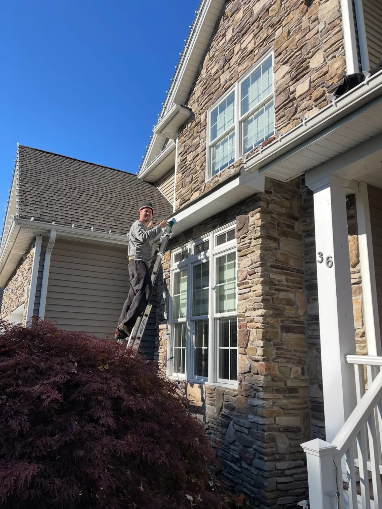 Brightline technician working from a ladder on a stone-front home